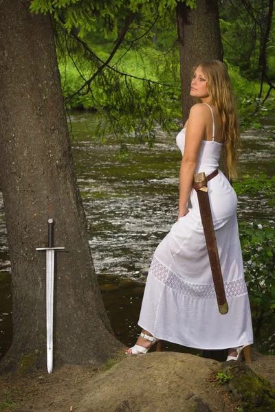 Schöne Frau im weißen Kleid mit Schwert in einem wilden Wald — Stockfoto