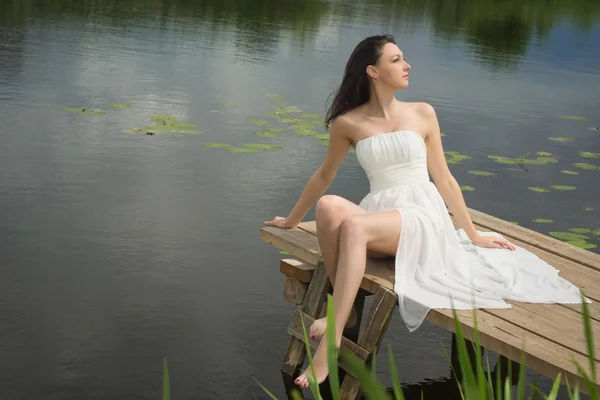 Розслаблююча молода жінка на дерев'яному пірсі біля озера — стокове фото