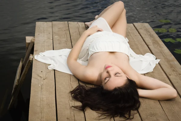 Relaxante jovem mulher no cais de madeira no lago — Fotografia de Stock