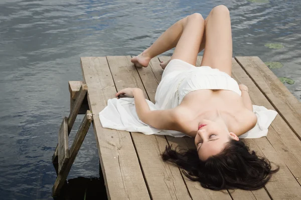 Pihentető fiatal nő a fa mólón-a tónál — Stock Fotó