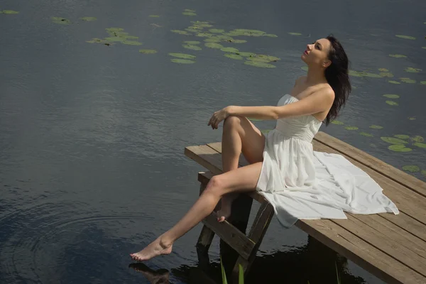 Relaxante jovem mulher no cais de madeira no lago — Fotografia de Stock