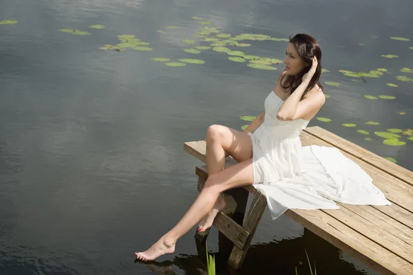 Relaxante jovem mulher no cais de madeira no lago — Fotografia de Stock