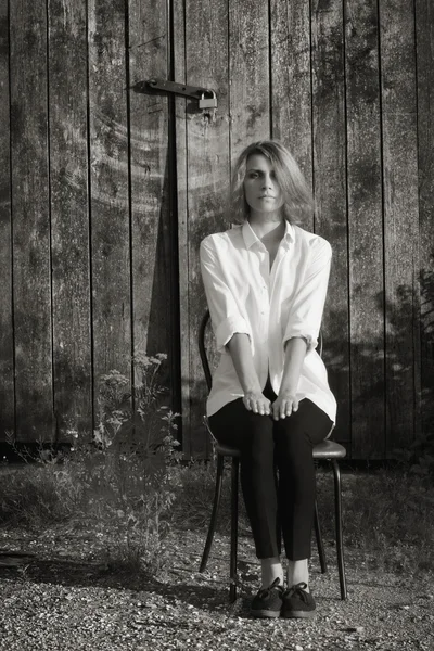Dívka sedící na židli proti pozadí dřevěná stodola — Stock fotografie