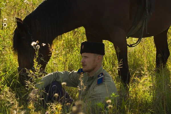 Русский казак с лошадью отдыхает в летнем поле — стоковое фото