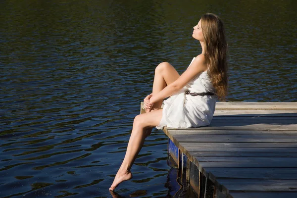 Relaxante jovem mulher no cais de madeira no lago — Fotografia de Stock