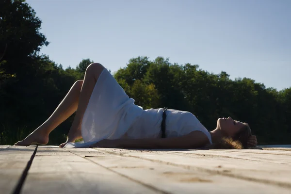 Relaxační mladá žena na dřevěném molu u jezera — Stock fotografie