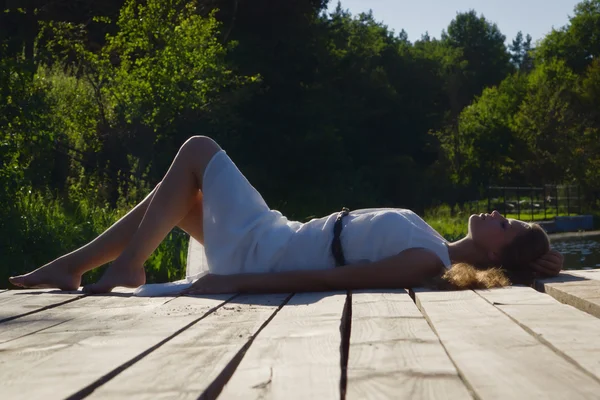 Расслабляющая молодая женщина на деревянном пирсе у озера — стоковое фото