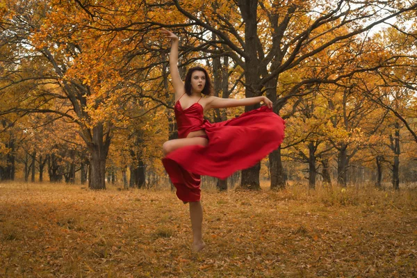 Дівчина в червоній сукні танцює в осінньому лісі — стокове фото
