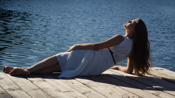 Relaxante jovem mulher no cais de madeira no lago — Fotografia de Stock