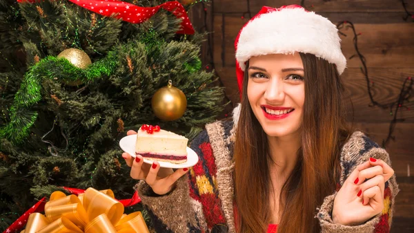 Красивая девушка сидит рядом с новогодней елкой и ест вкусный торт — стоковое фото