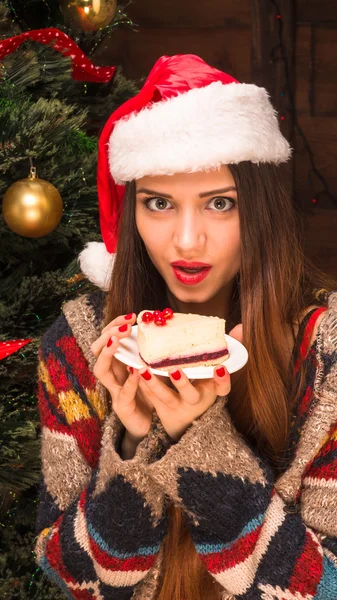 Beautiful girl sitting near New Year tree and eating delicious cake — Stock Photo, Image