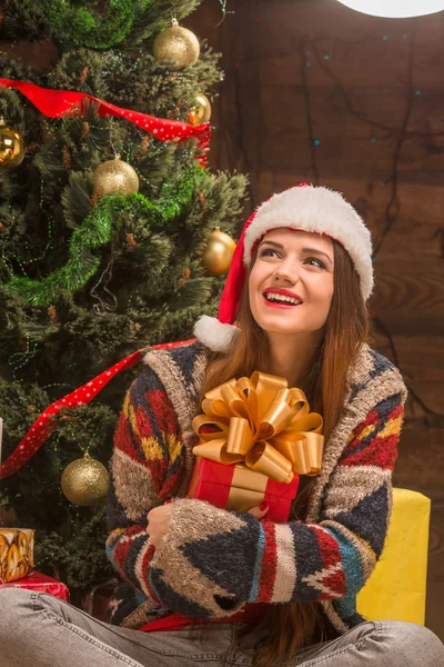 Beautiful girl sitting near New Year tree with a present — Stock Photo, Image