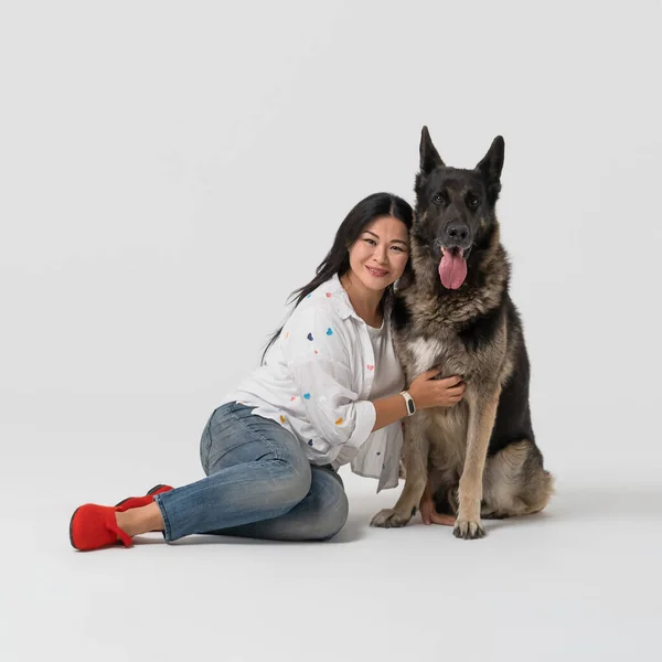 Piękna kobieta przytula rasowego psa pasterskiego. Szczęśliwa brunetka siedząca z psem na podłodze. Wycięte na białym tle — Zdjęcie stockowe