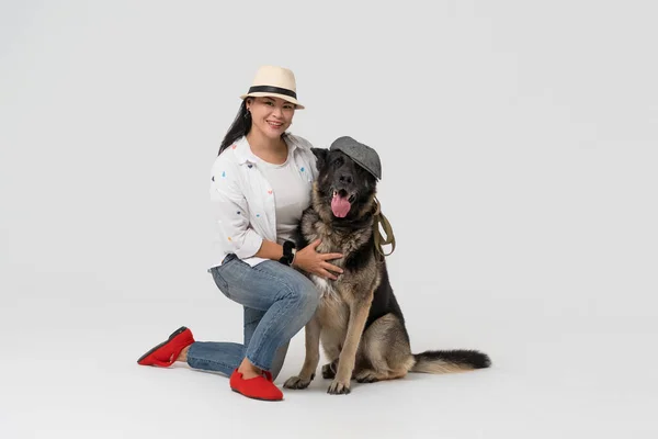 Funny Dog and hostess in hats. Woman in hat and Eastern European Shepherd wearing cap posing on white background. Pet concept — Stock Photo, Image