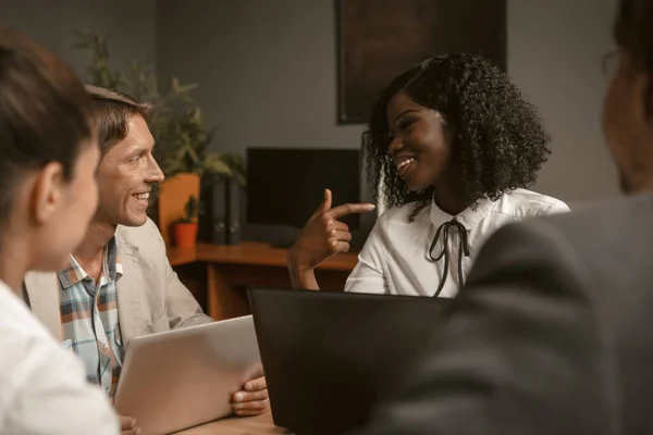 La gente divertida de negocios se ríe durante la reunión en la oficina. Trabajo en equipo de diversos grupos. Sonriente mujer afroamericana comunicándose con sus colegas. Imagen teñida — Foto de Stock