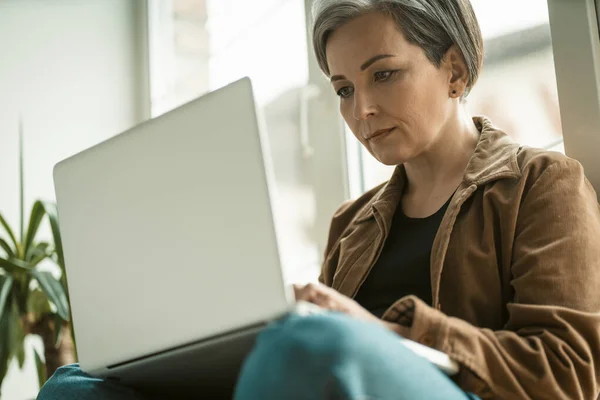 Blanke zakenvrouw werkt laptop computer zittend tegen het raam. Schot van onderen. Sluiten. — Stockfoto