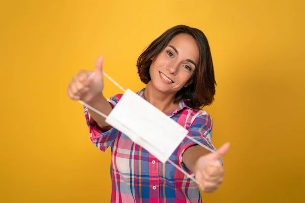 Mujer sonriente sostiene máscara protectora frente a ella. Corte sobre fondo amarillo. Concepto de cuarentena. Concepto de medidas preventivas o de protección —  Fotos de Stock