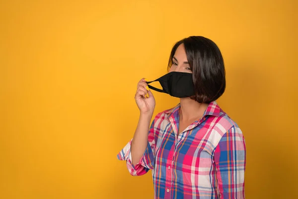 Mulher jovem bonito com máscara protetora facial durante a quarentena. Isolado em fundo amarelo. Conceito de surto de vírus — Fotografia de Stock