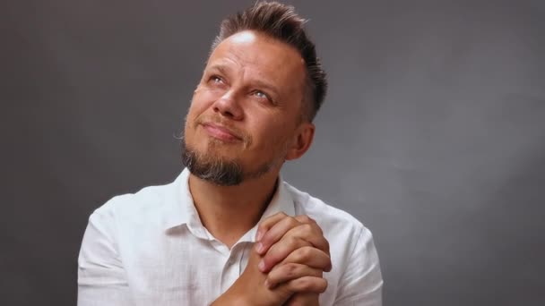 Un uomo adulto con la barba alza lo sguardo pensieroso, con le mani strette da una serratura. L'uomo medita in studio su uno sfondo isolato. Videocassetta. Alta qualità — Video Stock