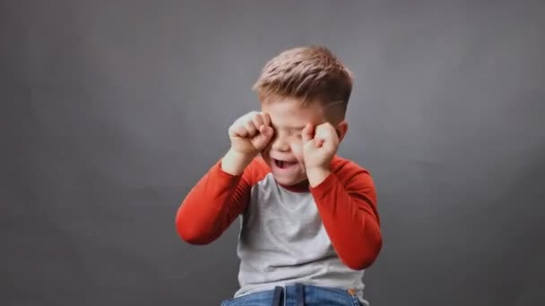 Jongen huilt in de studio tegen een geïsoleerde achtergrond. Jongen huilt en veegt tranen met zijn vuisten. Mobiele video. Hoge kwaliteit — Stockvideo