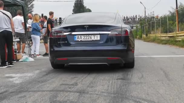Teslas siyah elektrikli araba yarış dışı. Arkasından arabaya bak. Adam bir sonraki arabayı imzalıyor. Mobil video. Arka planda seyirciler var. Yüksek kalite. 24 Ağustos 2020. Kyiv, Ukrayna — Stok video