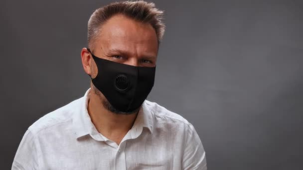 Middle-aged man in a medical mask shows his thumb up. Man in a protective mask nods his head against an isolated background. Mobile video. High quality. — Stock Video