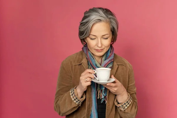 Wanita cantik elegan minum kopi atau teh memegang cangkir putih melihat di atasnya. Terisolasi di latar belakang merah muda dengan ruang fotokopi. Rekaman studio — Stok Foto