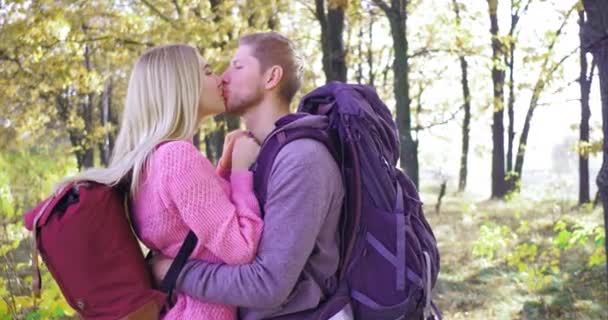Young couple of tourists in autumn forest on sunny afternoon. Blonde girl kisses and gently hugs her boyfriend. — Stock Video