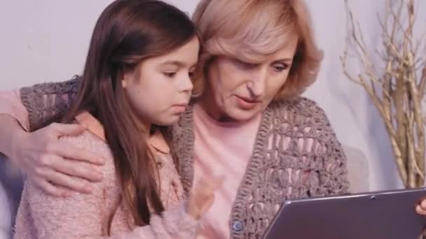 Großmutter und Enkelin sitzen am Laptop. Mädchen ist verängstigt und zeigt auf Monitor. Frau umarmt sie an den Schultern und schläft. — Stockvideo