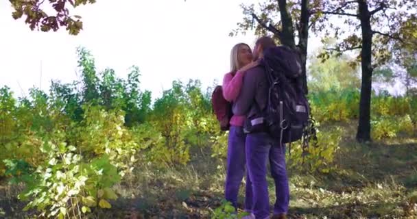 Молодая пара туристов в осеннем лесу в солнечный день. Блондинка нежно обнимает своего парня. Кавказский юноша целует ее. — стоковое видео