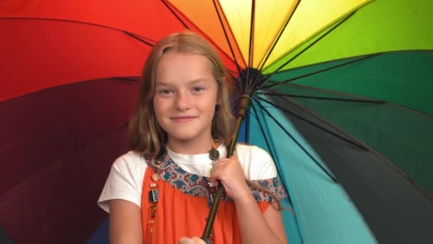 Usmívající se dívka v matčiných šatech s korálky zvraty rozevře pestrobarevný deštník. Bělošské dítě se dívá do kamery a usmívá se. Černé pozadí. — Stock video