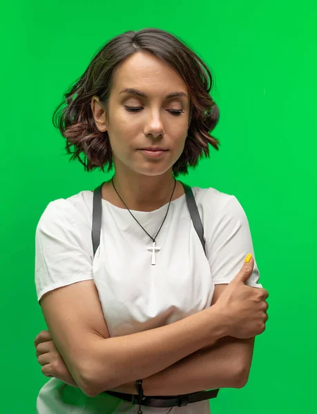 Mladá brunetka se dívá dolů se zkříženýma rukama. Veselý ženský model s krátkými tmavými vlasy izolované na chromakey nebo zelené pozadí. — Stock fotografie