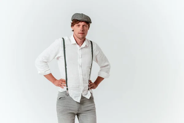 Jongeman met gevouwen handen op de romp. Mannelijke roodharige hipster in een cap en wit shirt met bretels. — Stockfoto