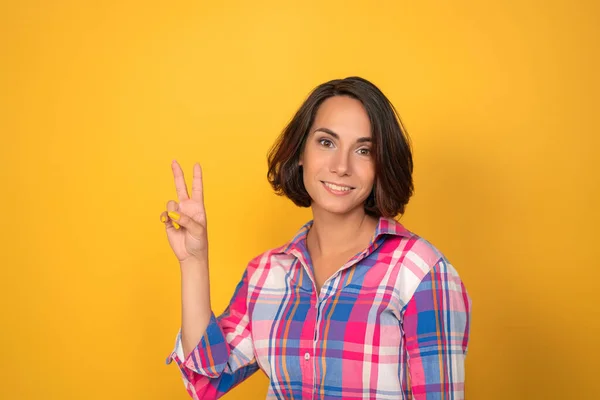 Jeune femme montre le signe de paix par ses mains sur fond jaune — Photo