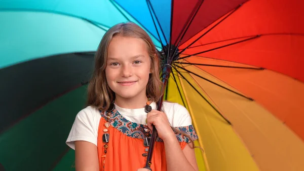 Fille souriante en robe de soleil de mères avec des perles tient ouvert parapluie multicolore lumineux. Enfant caucasien regarde caméra et sourit — Photo