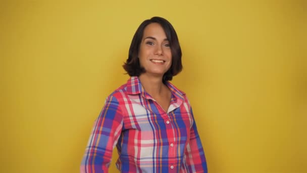 Junge kurzhaarige Frau mit dunklen Haaren auf gelbem Hintergrund steht auf und zeigt den Finger nach oben. Modell zeigt Daumen nach oben. — Stockvideo