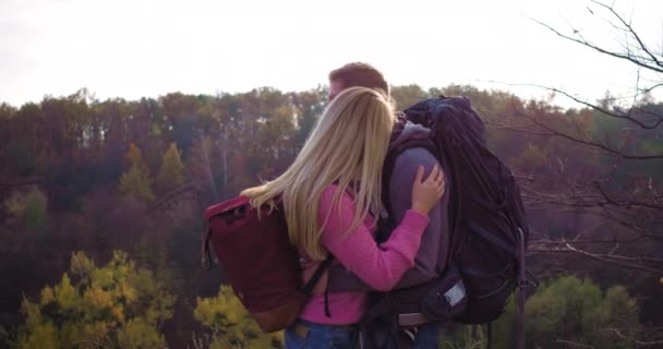 Fiatal pár turista áll szemben a háttérben a hegyek őszi erdőben a napsütéses délután. Megölelik egymást.. — Stock videók