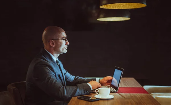 Biznesmen pracuje na komputerze w centrum biznesowym. Widok z boku pewny siebie biały człowiek używa laptopa siedzi przy drewnianym stole z filiżanką kawy i telefon komórkowy na nim. Koncepcja biznesu. Przestrzeń kopiowania — Zdjęcie stockowe