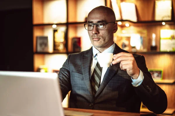 Udany biznesmen czyta wiadomości ze światów. Mężczyzna w średnim wieku patrzy na ekran laptopa pijąc kawę podczas pracy w centrum biznesowym lub kawiarni hotelowej — Zdjęcie stockowe