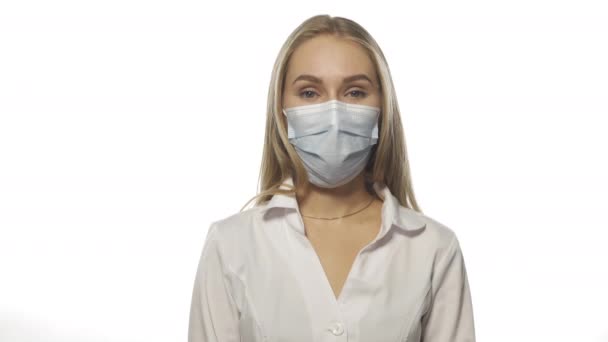 Ung sjuksköterska i en medicinsk mask visar likgiltighet med sina axlar eller inte vet information, tittar på kameran. Isolerad på vit bakgrund. Högkvalitativ 4k-upplösning — Stockvideo