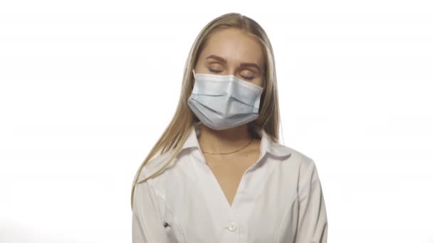 Enfermera cansada o descuidada con máscara protectora y bata de hospital médica mirando a la cámara aislada en blanco. Imágenes de resolución 4k de alta calidad — Vídeo de stock