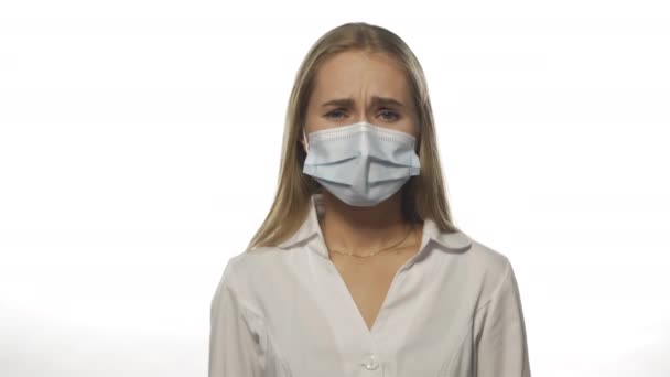 Egy orvosi maszkot viselő nővér felfedi, hogy a por tünetei a kamerába néznek orvosi köpenyben és lila eldobható kesztyűben. Elszigetelve, fehér háttérrel. 4k felbontású felvételek — Stock videók