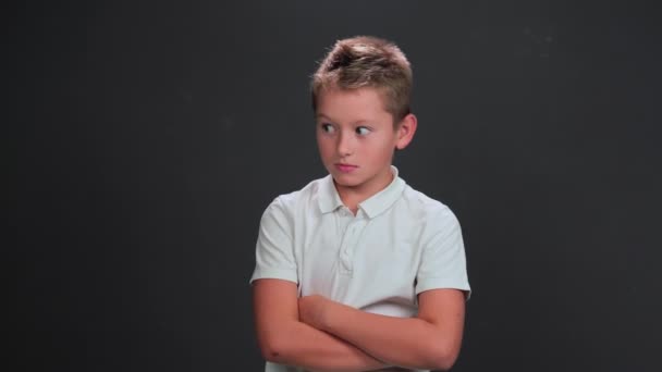 Caucasian 10 years boy looks side ways in surprise or terrified. Child with his arms folded poses on black background. Surprise or scare concept — Stock Video