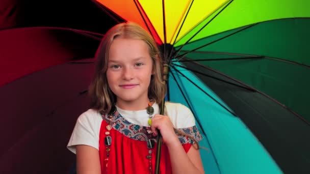 Little girl 8 -10 years old holding colorful rainbow umbrella in the studio looking at the camera isolated on dark gray or black background. High quality footage — Stock Video