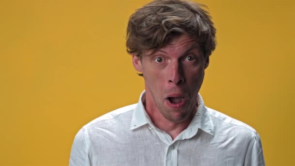 Young man making funny silly facial emotions isolated on yellow background. Weird dorky face of a handsome young man in white shirt. High quality 4k resolution footage — Stock Video