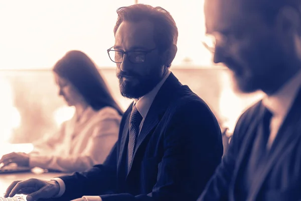 Gente de negocios trabajando en oficinas de espacio abierto. Los colegas masculinos se comunican entre sí sentados en el mismo escritorio. Concepto de trabajo en equipo. Vista lateral. Imagen tonificada — Foto de Stock