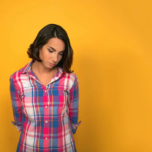 Young Sad pensive woman feels guilty, thinks looking down while standing against of yellow wall in background with copy space on right side — Stock Photo, Image