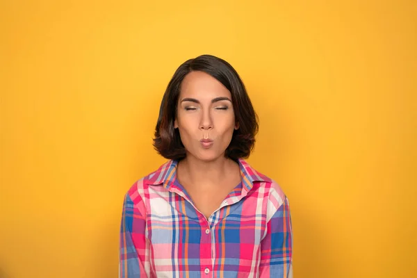 Mujer joven haciendo caras graciosas mirando a la cámara. Modelo femenino en camisa a cuadros aislada sobre fondo amarillo. Emociones humanas, concepto de expresión facial —  Fotos de Stock