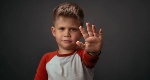 Liten pojke i röd skjorta olycklig visar stopp med handen isolerad på grå bakgrund. Mänskliga känslor, ansiktsuttryck. Ansiktsuttryck, känslor, känslor — Stockfoto