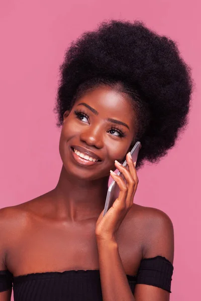 美丽的非洲裔美国女人在电话或智能手机上交谈，有着漂亮的非洲式发型，站在黑色肩膀上微笑，顶部被粉色背景隔开 — 图库照片
